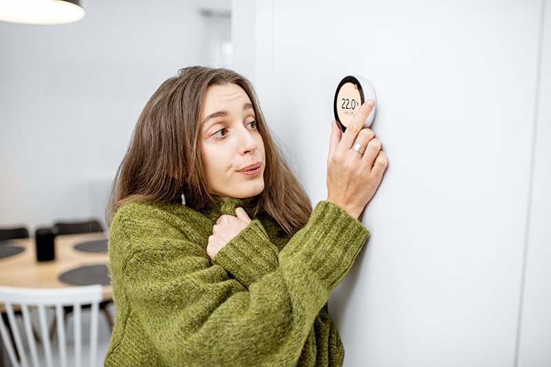 woman in sweater turning up thermostat.