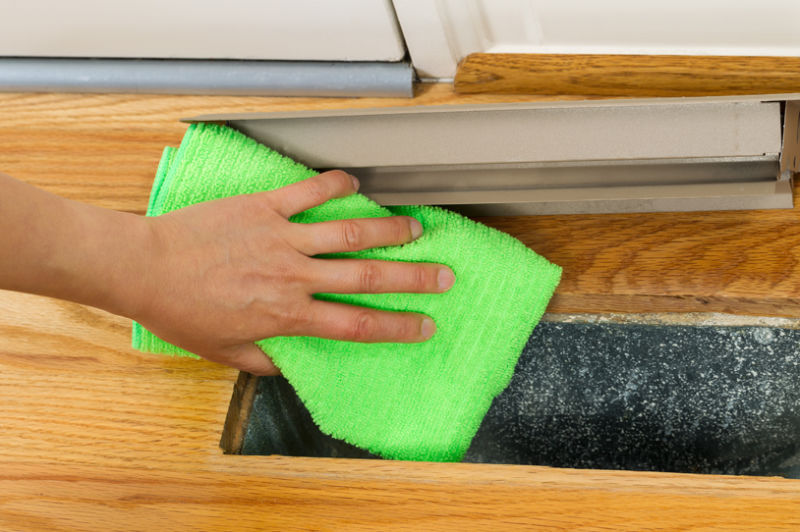 Air Duct Cleaning Reminders. Person cleaning air duct with green rag.